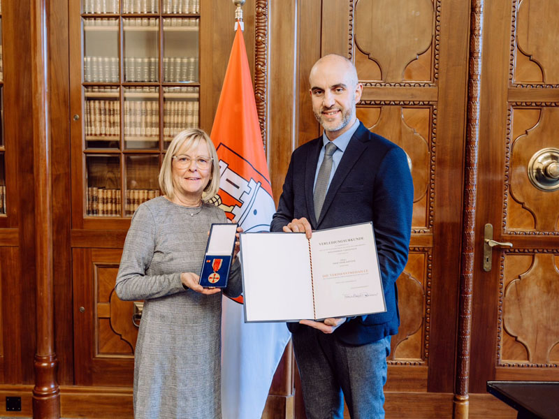 Imme Sierk-Krüger und Belit Onay halten das Verdienstkreuz und die Ehrenurkunde